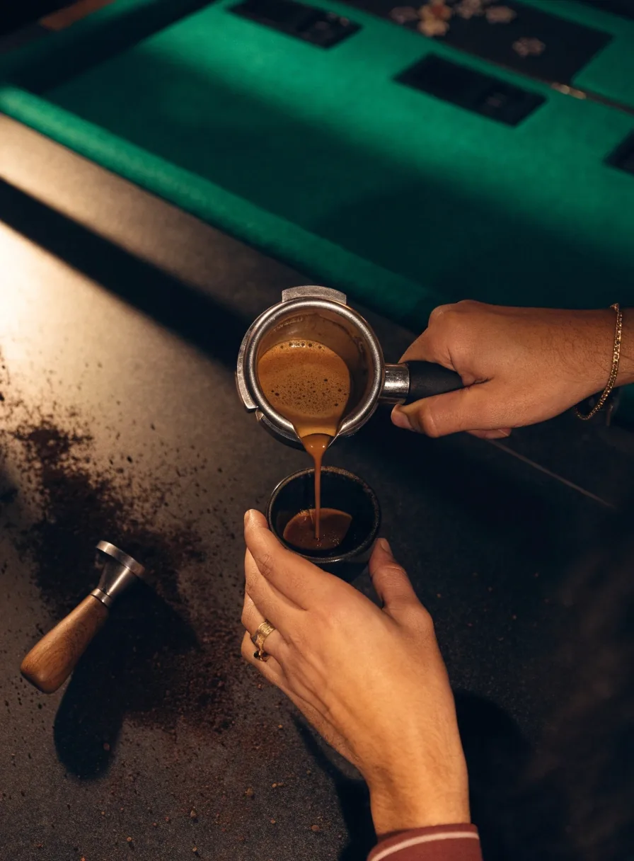 Ręce baristy przelewające espresso do filiżanki na ciemnym blacie lady